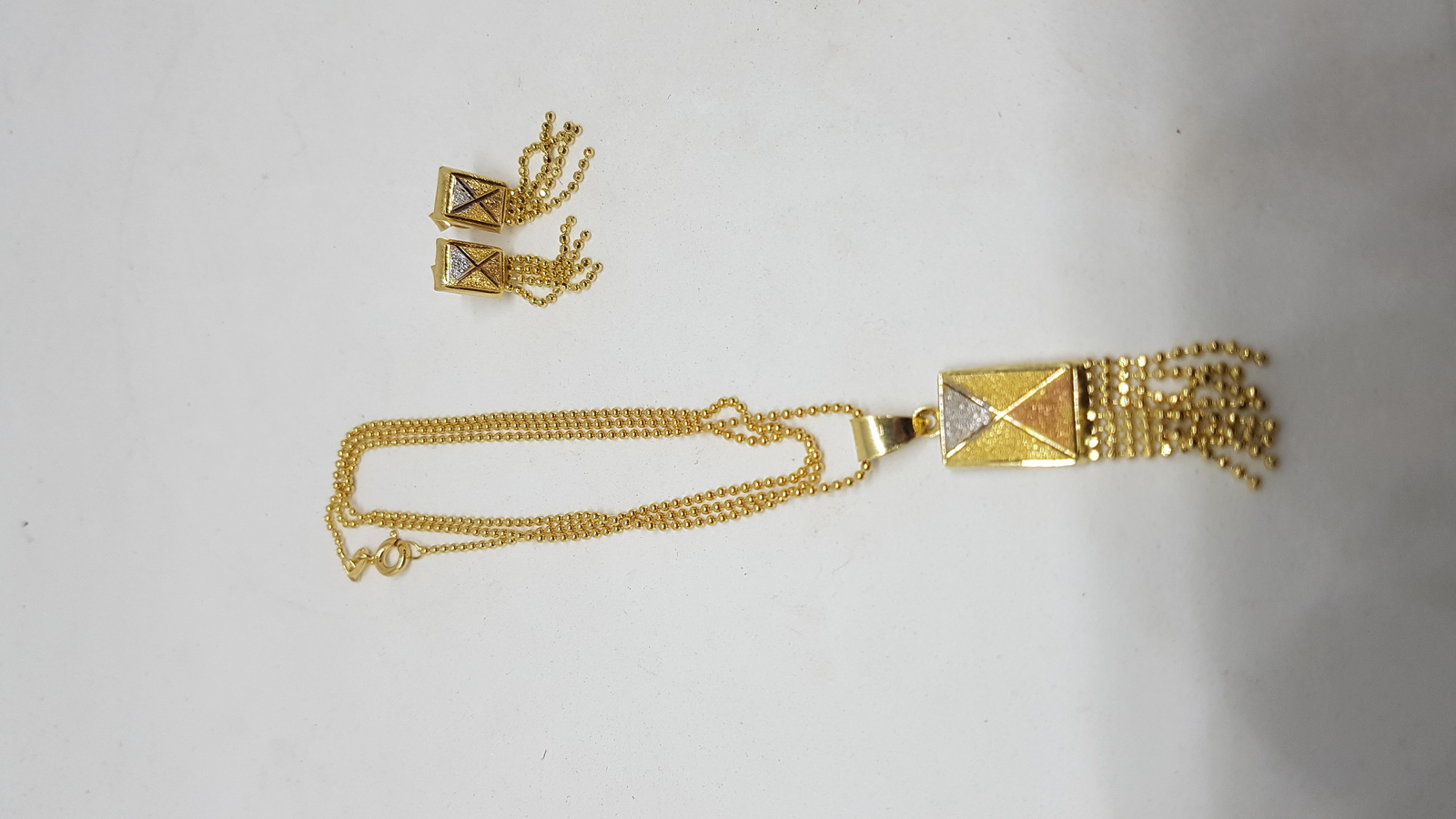 Discover our tri-coloured yellow metal pendant and earring suite. Textured with white and rose accents, it's a luxurious addition to any outfit. Explore now for a unique style boost!